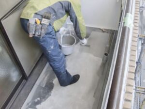 バケツと刷毛でベランダ防水工事をする職人